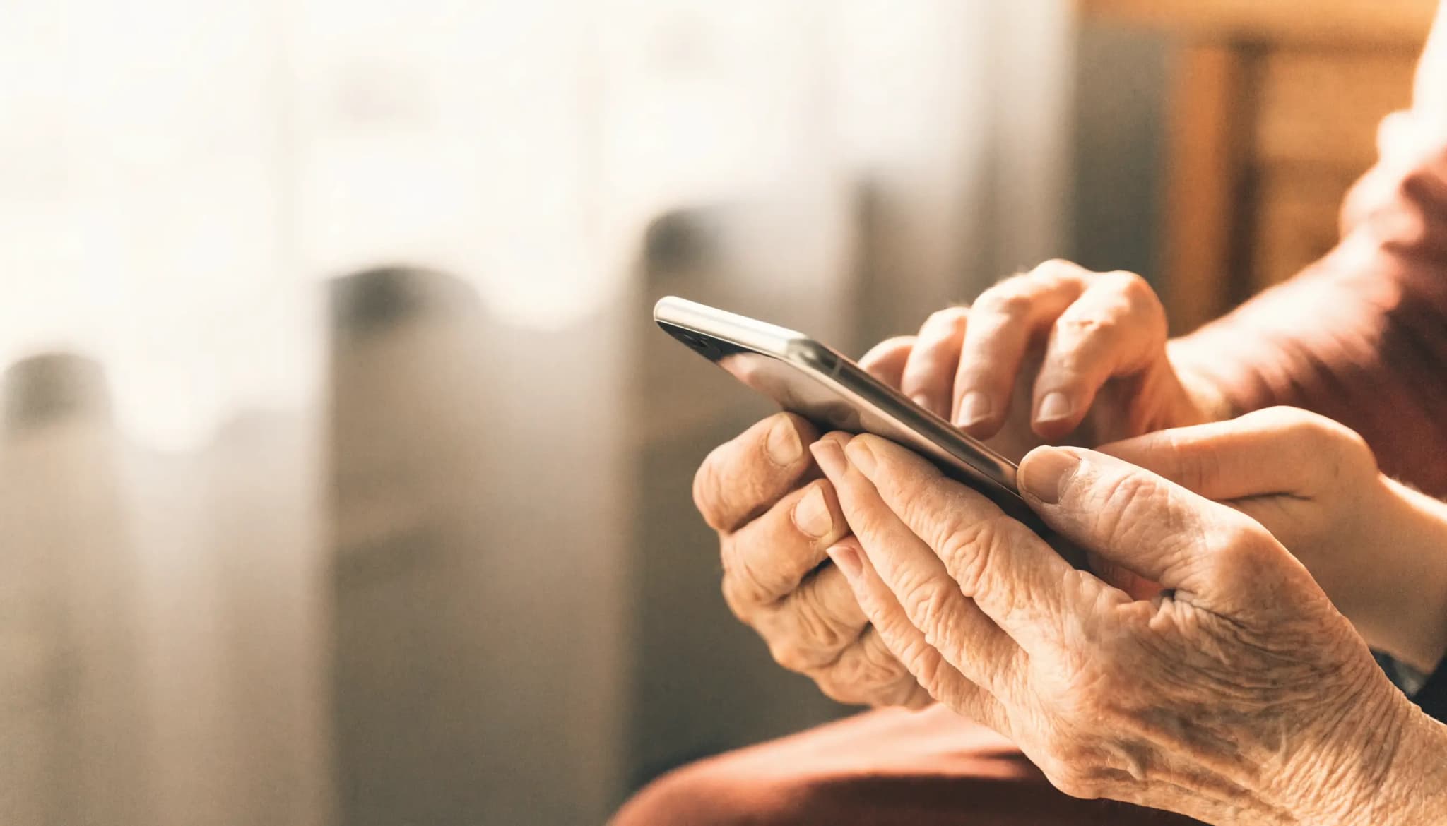 Eine jüngere und eine ältere Hand gemeinsam an einem Smartphone, warmes Licht